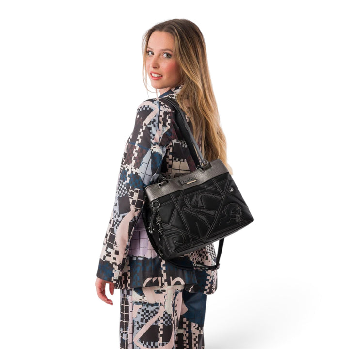 ada-shoes.ro Anekke handbag in black with metallic details, worn over the shoulder by a woman in a patterned suit.