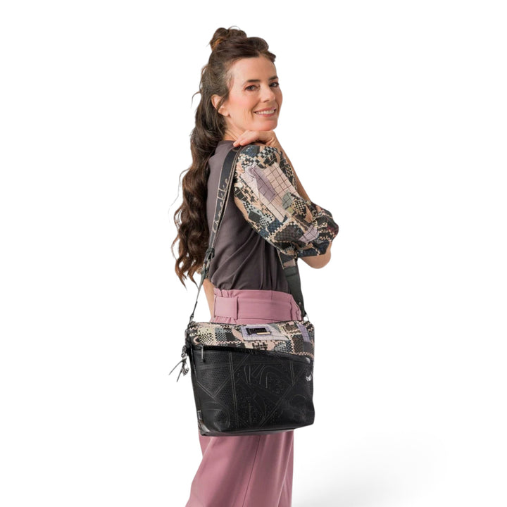 Woman wearing an Anekke crossbody bag with black and patterned panels, featuring an adjustable strap and zipper.