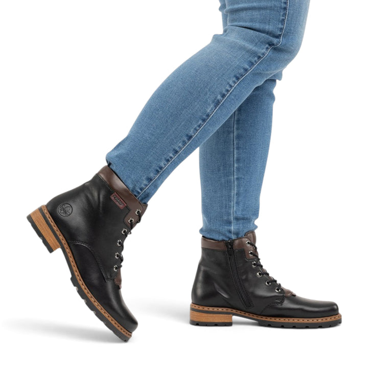 ada-shoes.ro Rieker black faux leather ankle boots with brown accents, side zipper, and robust lug sole on a model